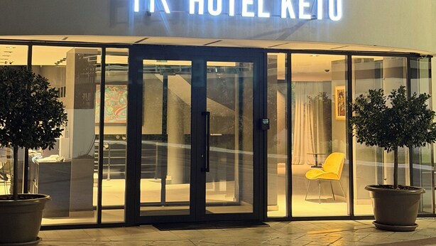 El exterior del Hotel HK Keto, con una fachada moderna, grandes puertas de cristal y plantas en macetas al frente.