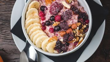 A bowl of oatmeal with fruits and nuts on a plate with a spoon.