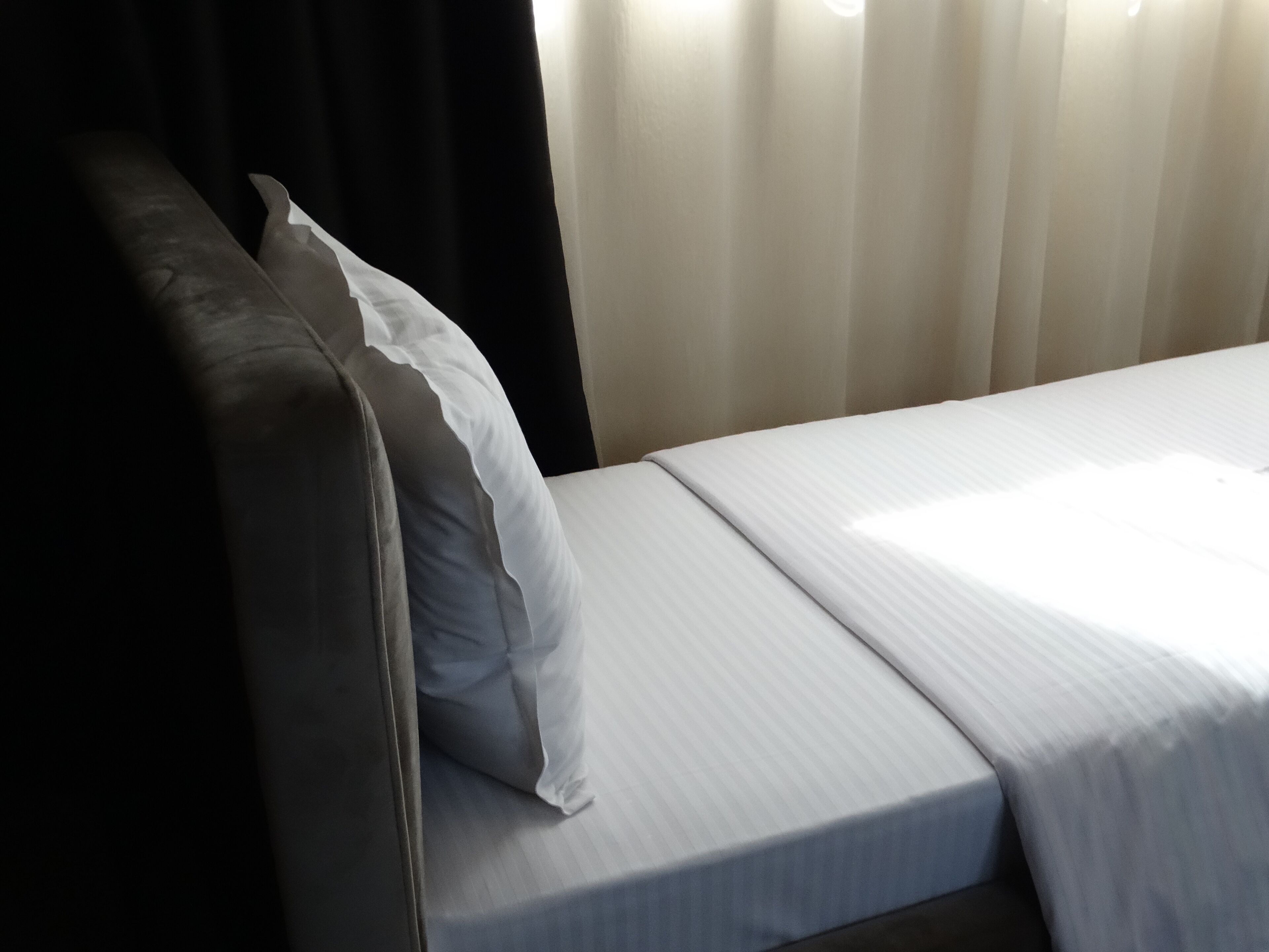 A hotel room with a bed, a pillow, and a curtain.