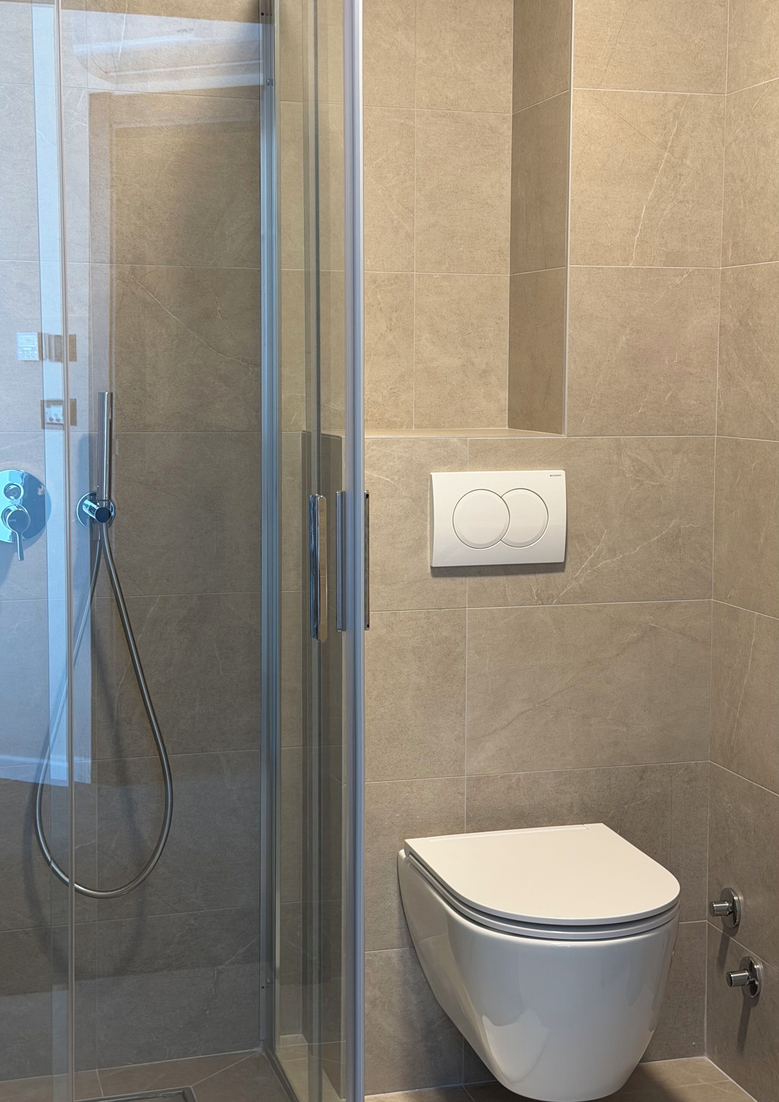 A bathroom with a glass-enclosed shower, a toilet, and a wall-mounted control panel.