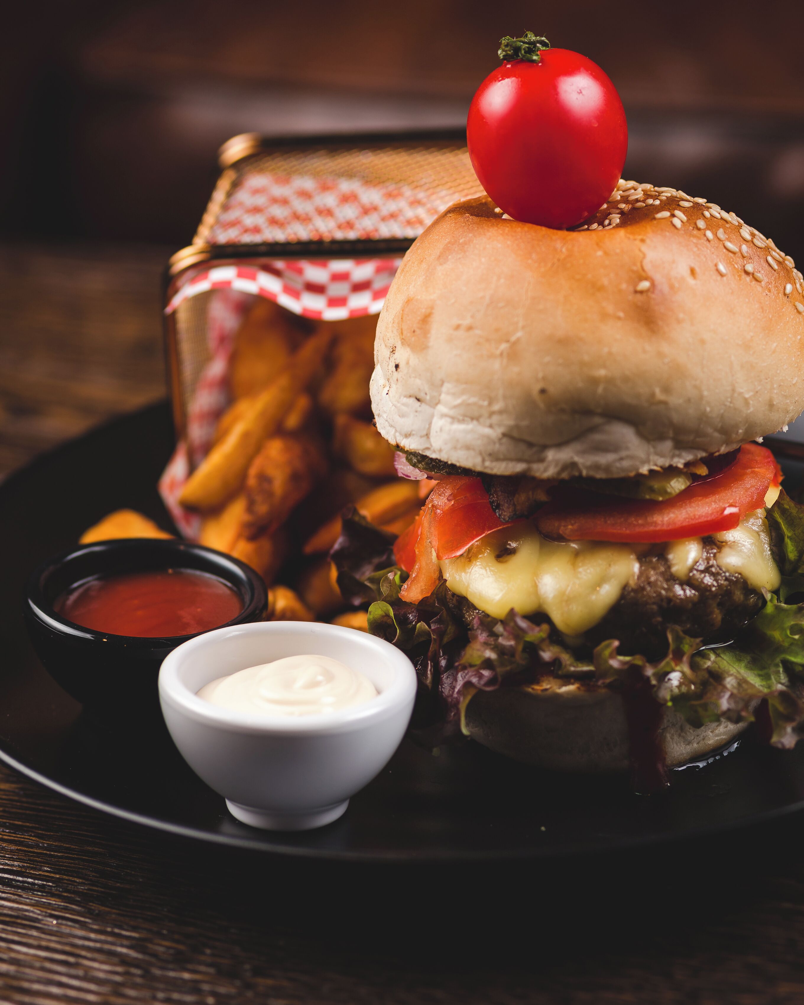 A burger with a tomato on top, accompanied by fries and two dipping sauces.