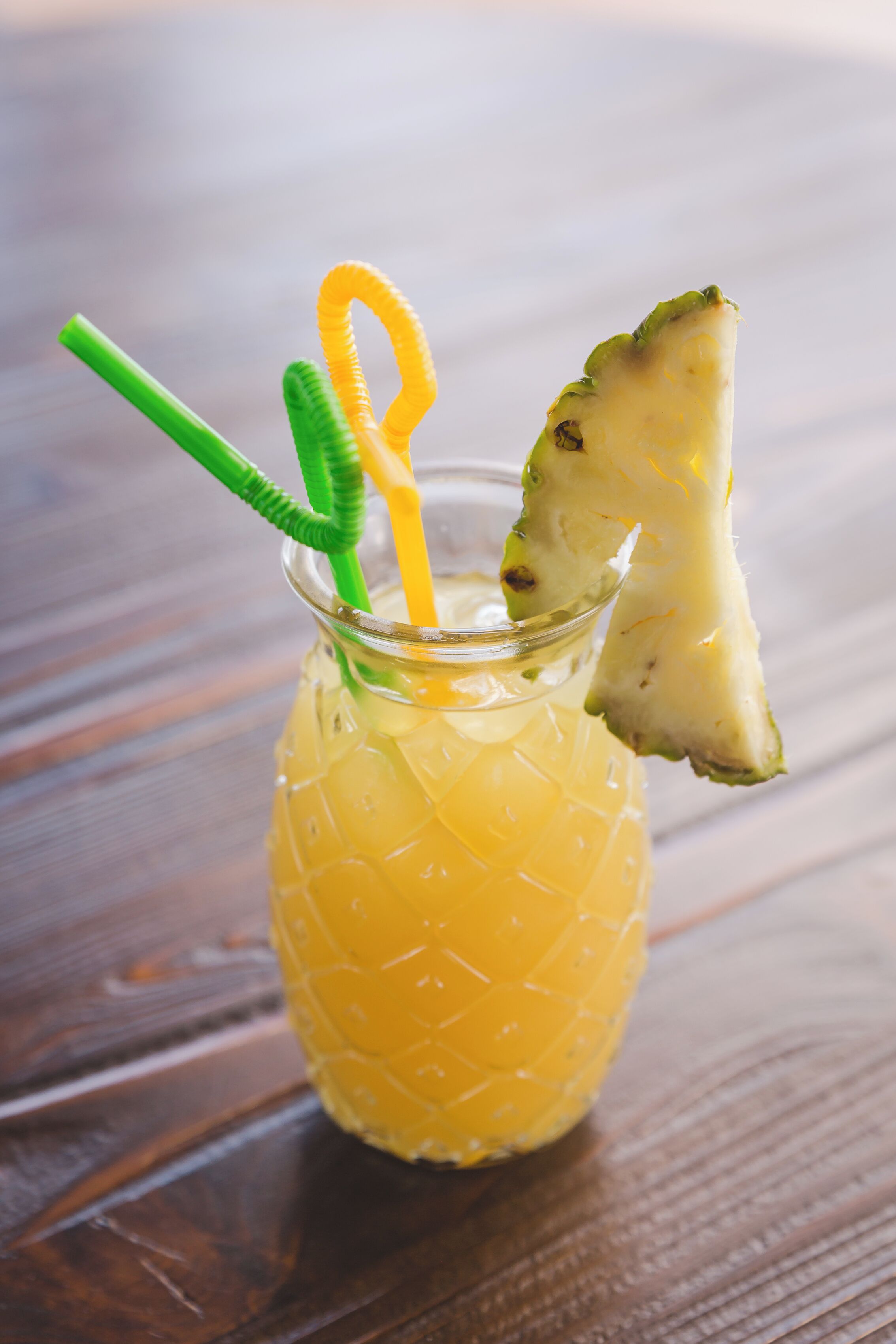 Un vaso con un diseño texturizado, una pajita verde y un trozo de piña.