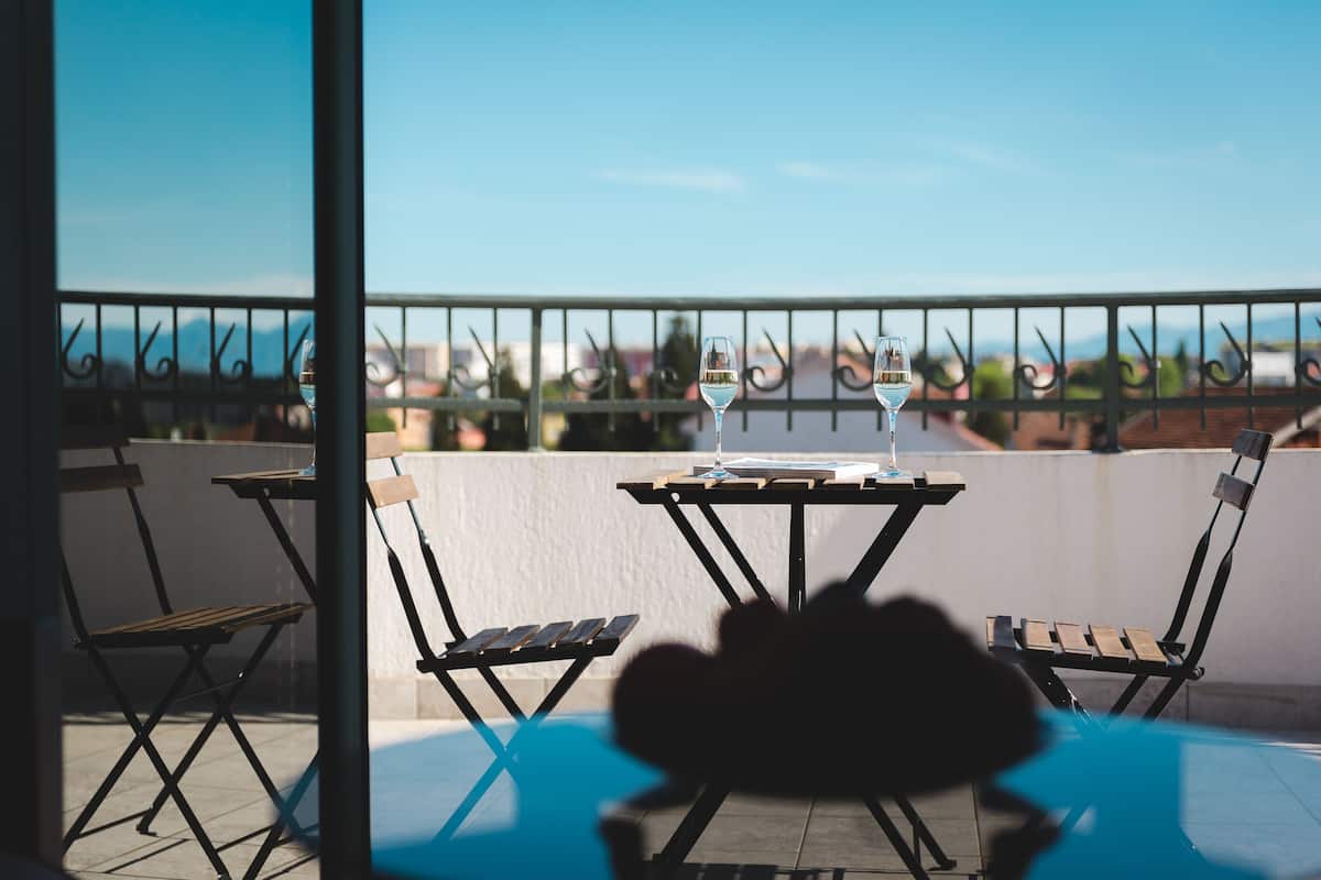 A balcony with a table and two chairs, a glass of wine, and a view of the cityscape.
