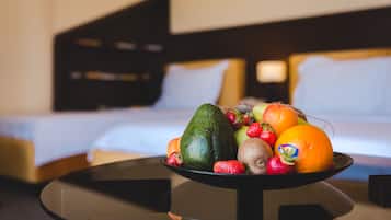 Uma tigela de frutas sobre uma mesa, com uma cama e cabeceira ao fundo.