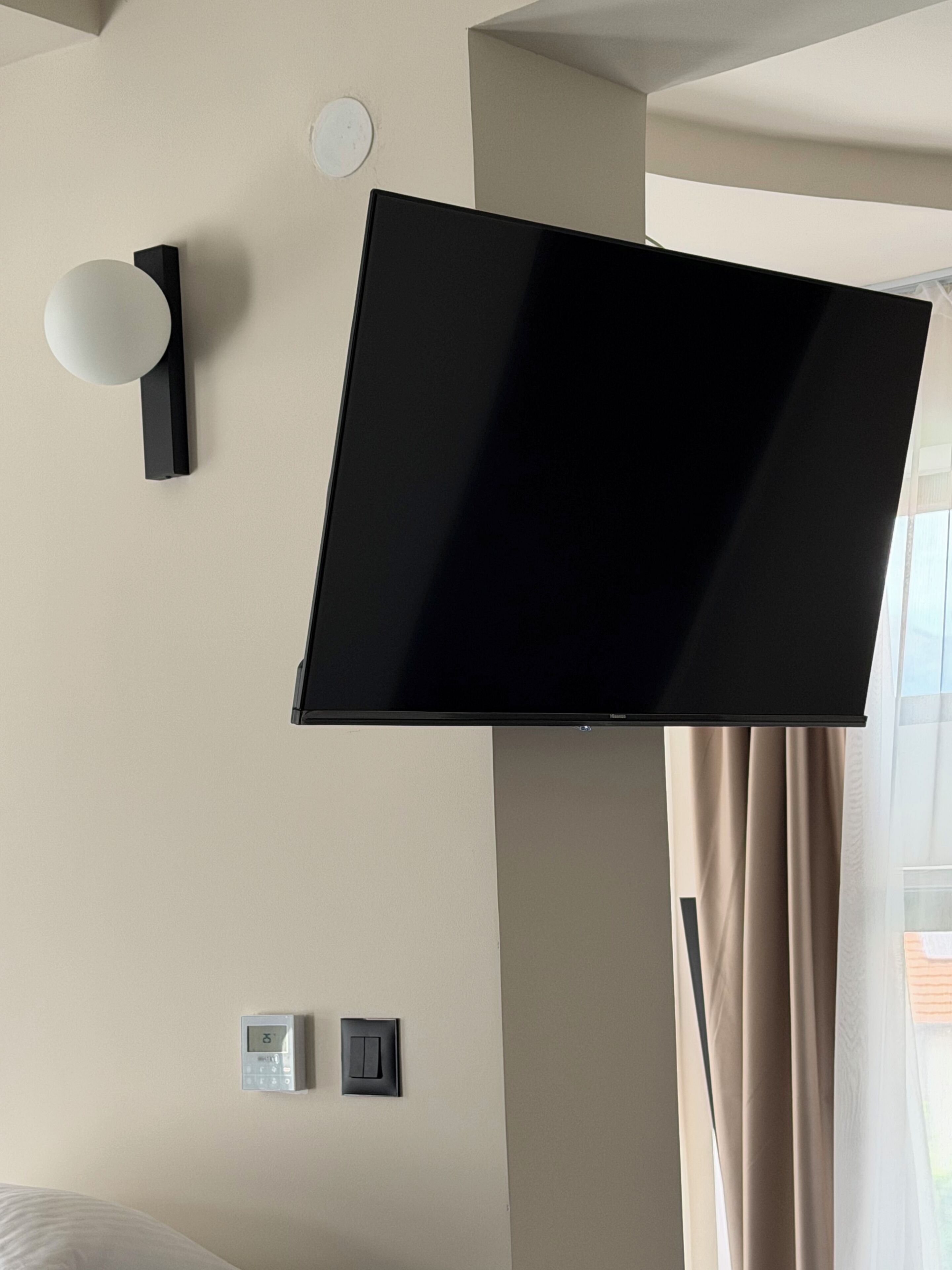 Una camera d'albergo moderna con una TV a schermo piatto montata a parete, un termostato e un interruttore della luce.