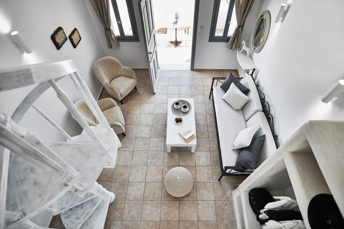 A modern, well-lit living room with a sofa, armchair, and coffee table. A large window provides natural light, and a door leads to an outdoor area.