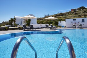 Relax by the serene pool surrounded by lush greenery and a picturesque hillside view.