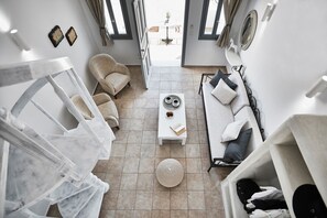 Relax in a spacious living area with a sofa, chairs, and ottoman, featuring a shelving unit and a large window with a view.