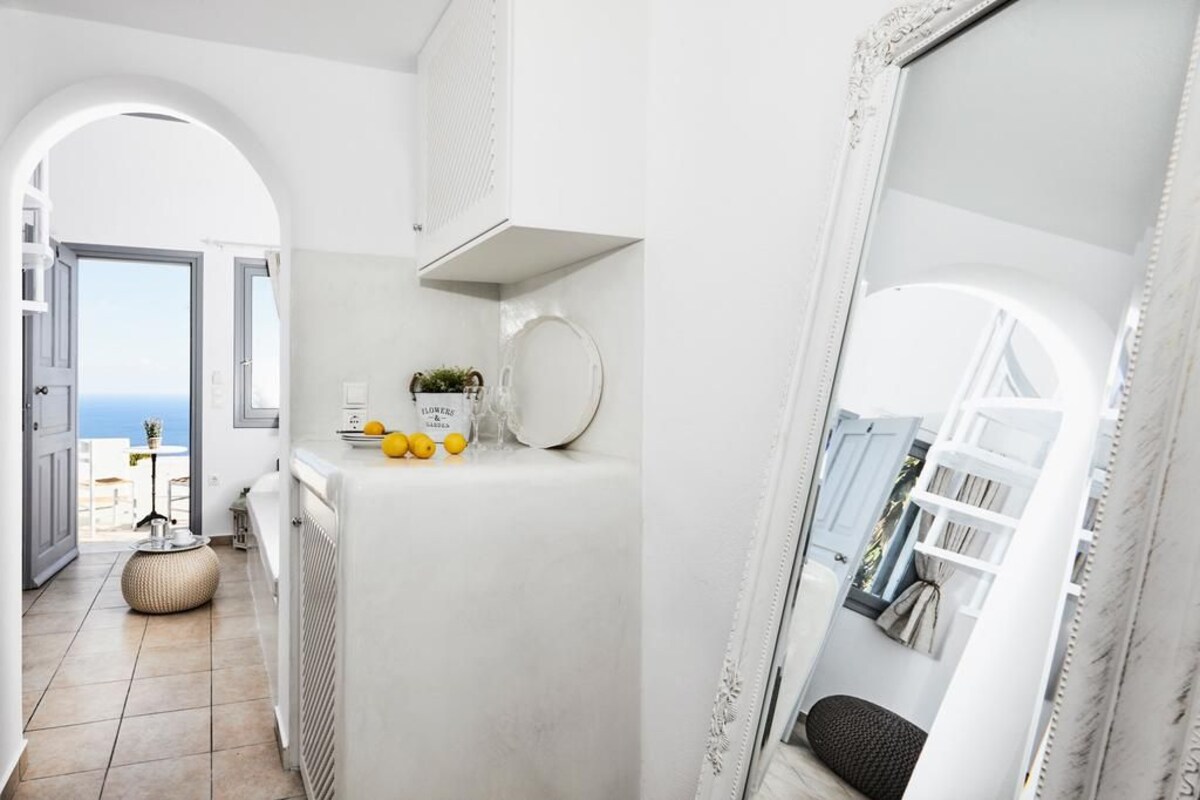 A modern, white interior with a kitchen area, a round mirror, and a view through an open door.