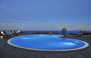 A swimming pool with lounge chairs and a decorative metal sculpture, surrounded by a tiled deck and overlooking a body of water.