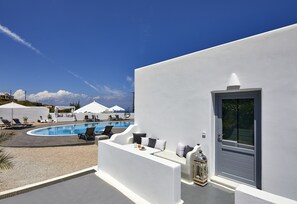 A white building with a pool, outdoor seating, and umbrellas.