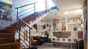 Una escalera conduce a una zona de bar con piso de madera, una barra con caja registradora y diversas decoraciones en las paredes, incluyendo diplomas y fotografías enmarcadas.