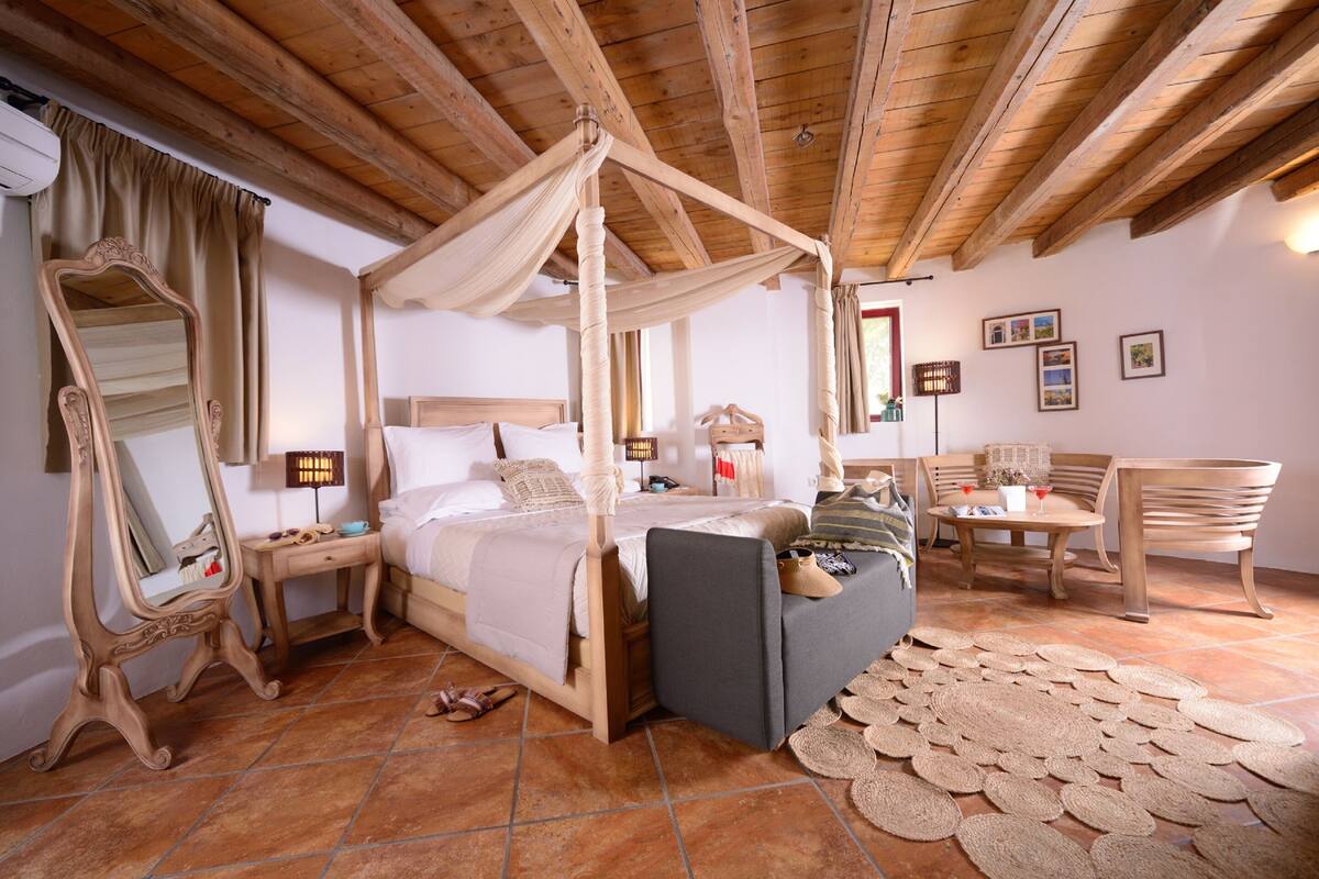A bedroom with a four-poster bed, a large mirror, a bedside table, a chair, a small table with a lamp, and a rug.