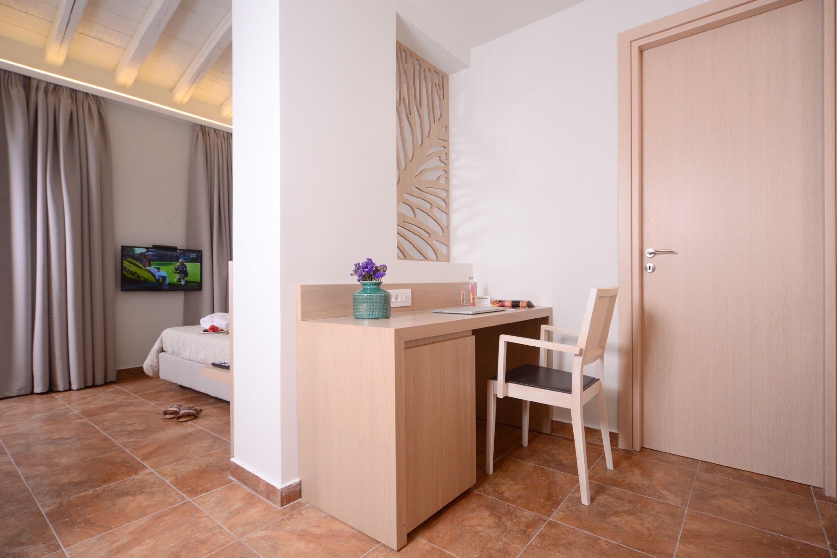Un dormitorio con cama, escritorio, silla, televisor y puerta.