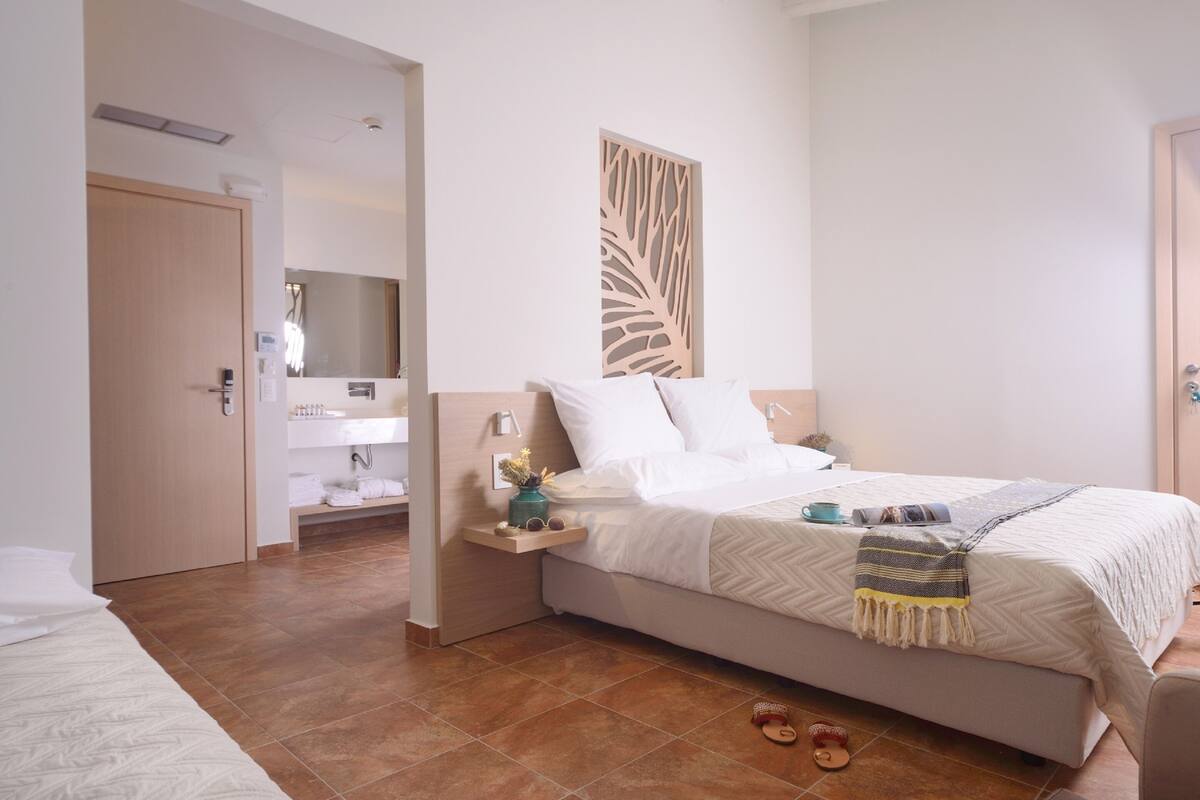 A hotel room with a bed, a bedside table, a mirror, and a bathroom visible through an open door.