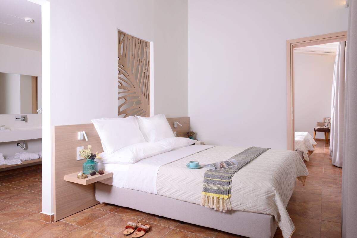 A modern bedroom with a large bed, a bedside table with a lamp, a small plant, and a mirror.