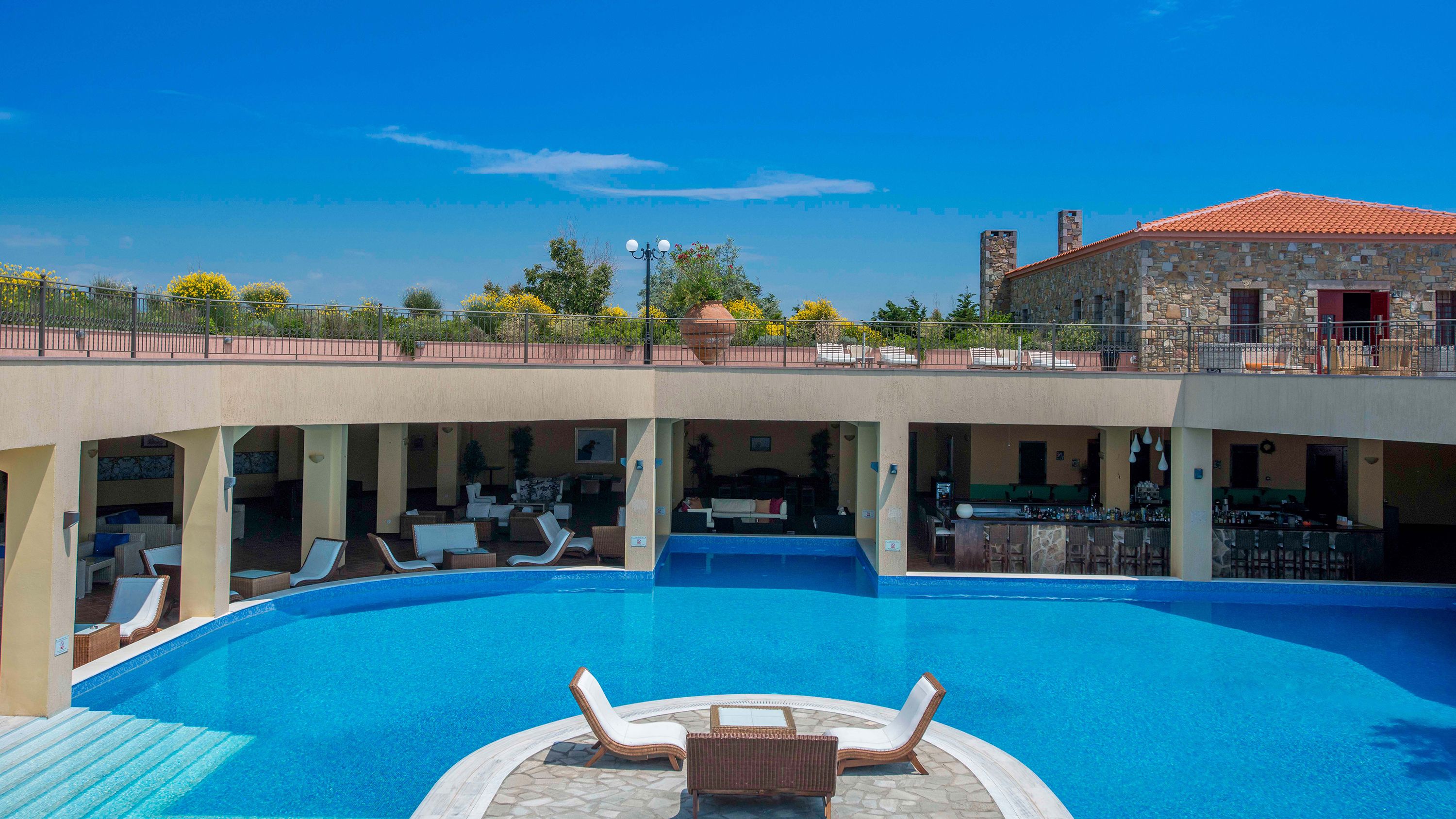 A hotel with a large outdoor swimming pool, multiple lounge areas, and a bar.