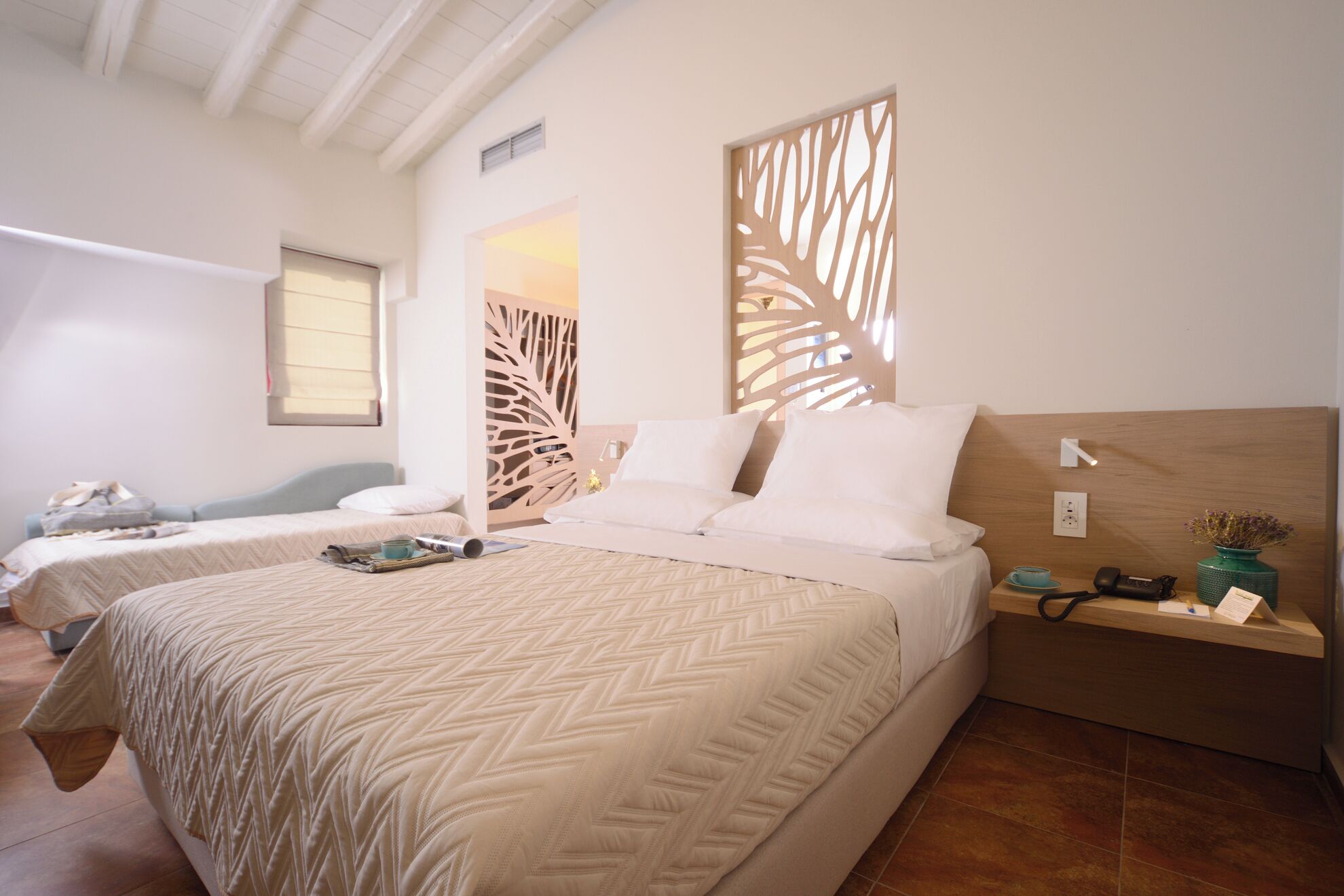 Quarto de hotel com duas camas, cabeceira de madeira, mesa de cabeceira com abajur e painel decorativo na parede.