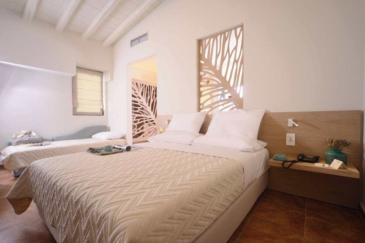 A hotel room with two beds, a wooden headboard, a bedside table with a lamp, and a decorative wall panel.