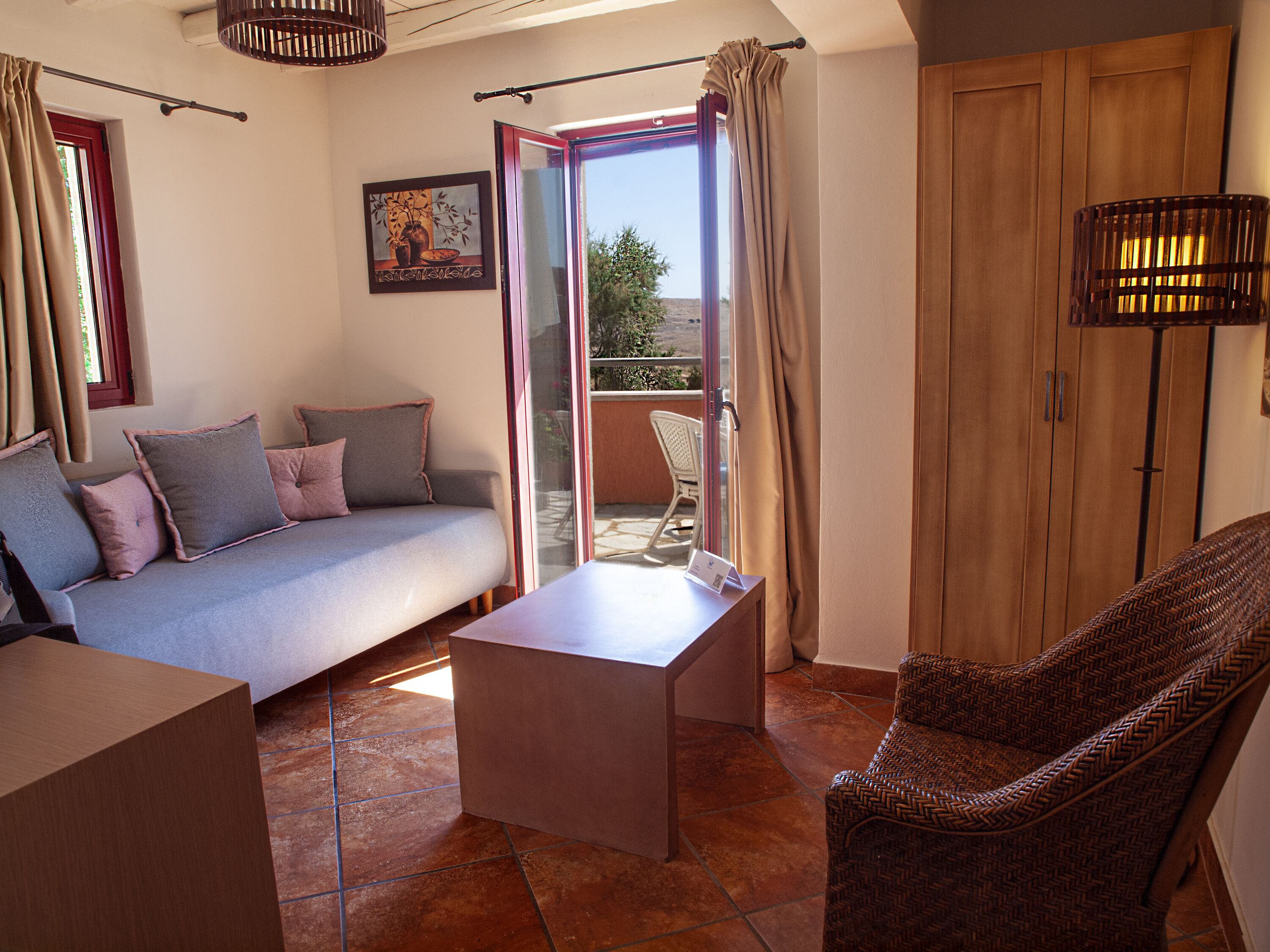 A cozy living area with a sofa, a small table, and a wicker chair. A sliding glass door leads to an outdoor patio.
