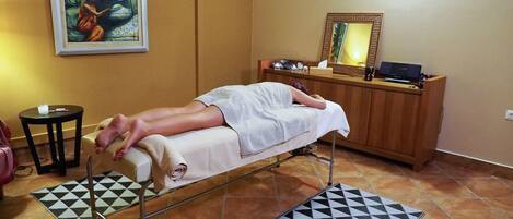 A room with a massage table, a small round table with a candle, a mirror, and a wooden cabinet.