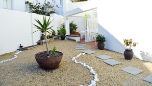 A courtyard with potted plants, a seating area, and a white wall. - Small Bay Guest House (Cape Town)