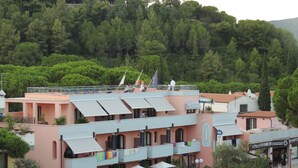 Un hotel de varios pisos con balcones, mobiliario exterior y vistas a una ladera boscosa.