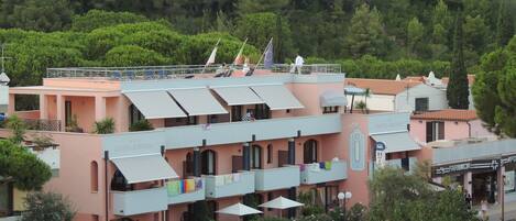 A multi-story hotel with balconies, outdoor seating, and a view of a forested hillside.