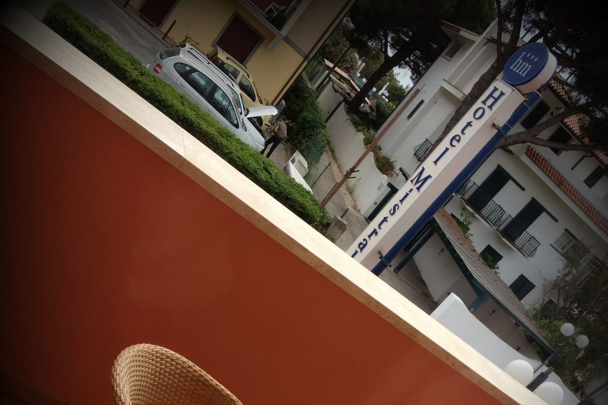 Un balcón con sillas de mimbre y una mesa, con vista a un edificio que tiene un letrero que dice 'HOTEL'.