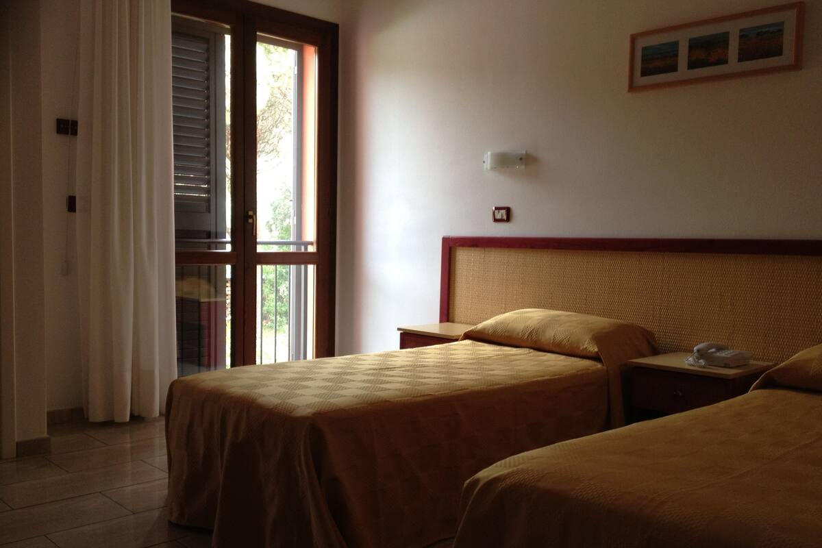 Habitación de hotel con dos camas, una ventana con cortinas, una mesita de noche con teléfono y una lámpara fijada a la pared.