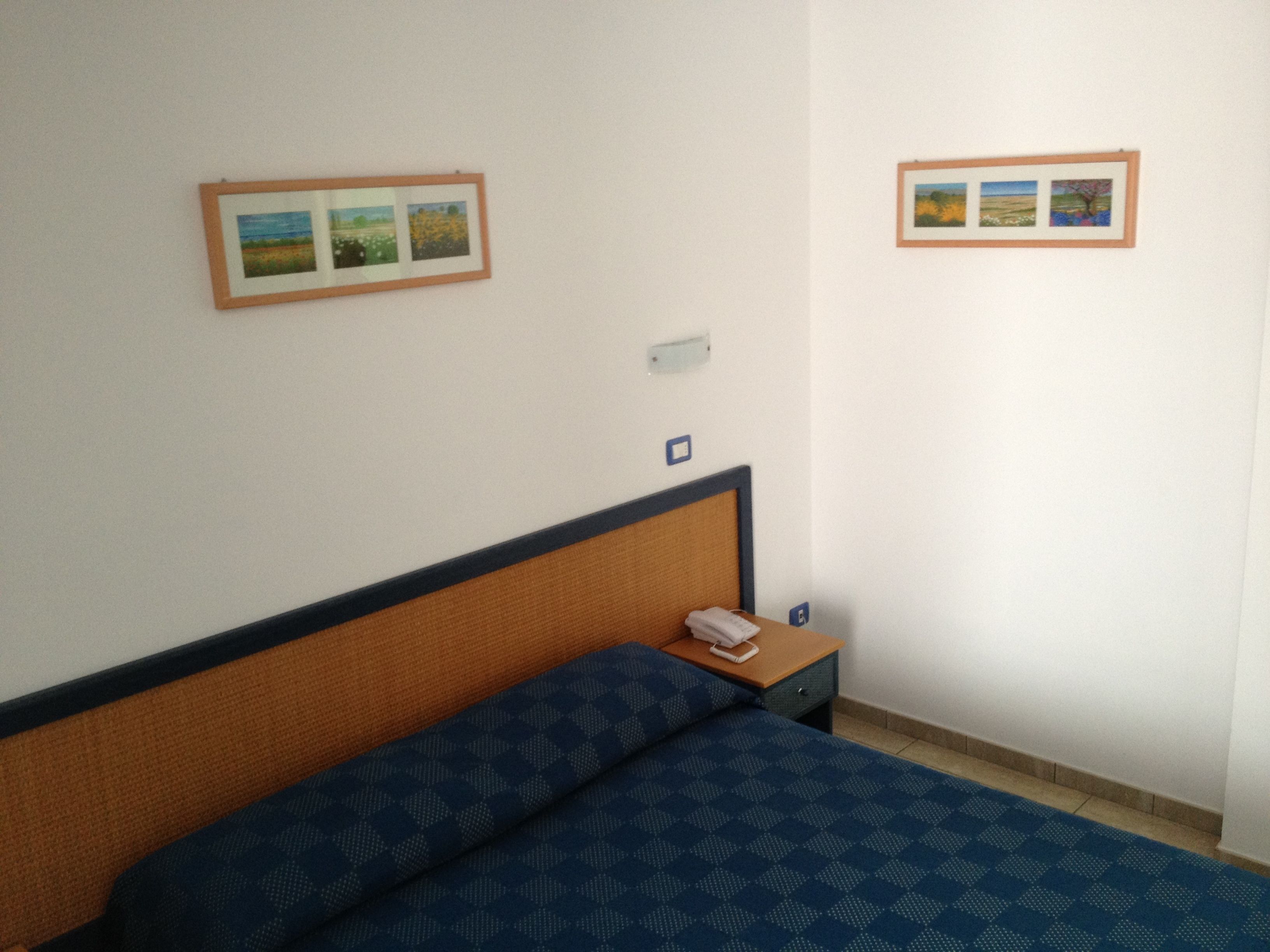 Ett hotellrum med en säng, ett nattduksbord med en telefon och två inramade tavlor på väggen.