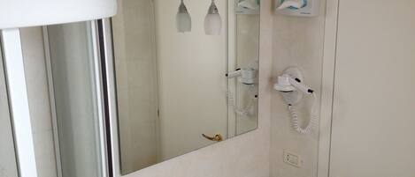 A bathroom with a sink, mirror, hairdryer, and towel dispenser.