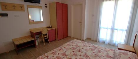 A bedroom with a bed, a desk, a chair, a wardrobe, a television, and a window with curtains.