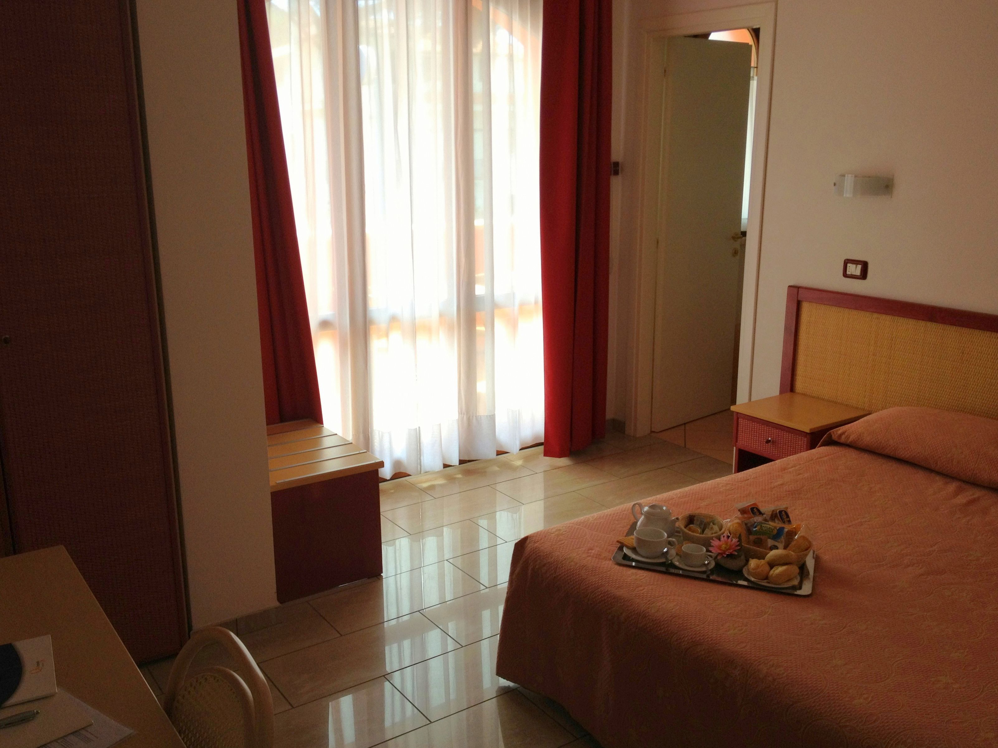 A hotel room with a bed, a bedside table, a desk, and a window with curtains.