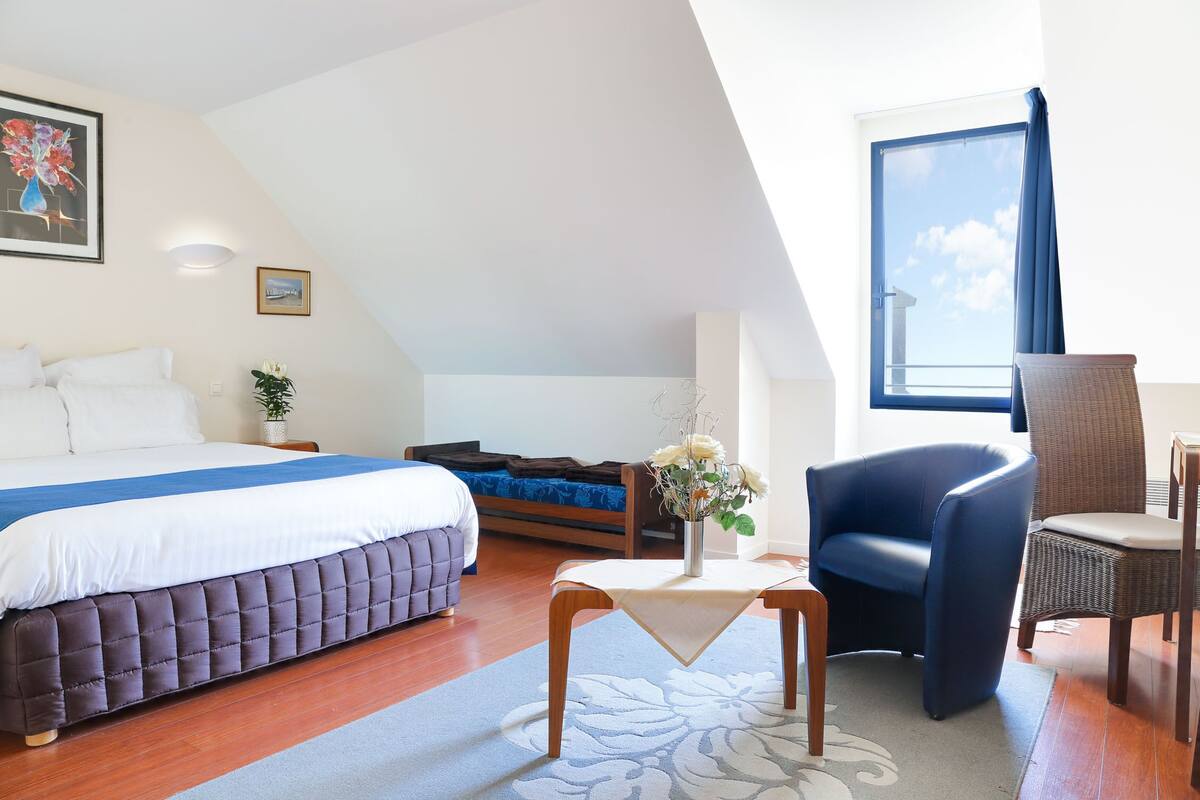 A bedroom with a bed, a chair, a table, and a window with curtains.