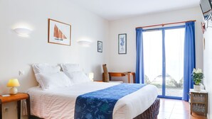 A bedroom with a bed, a desk, a chair, and a window with curtains. - Hôtel le Chevalier Gambette (Saint-Armel)