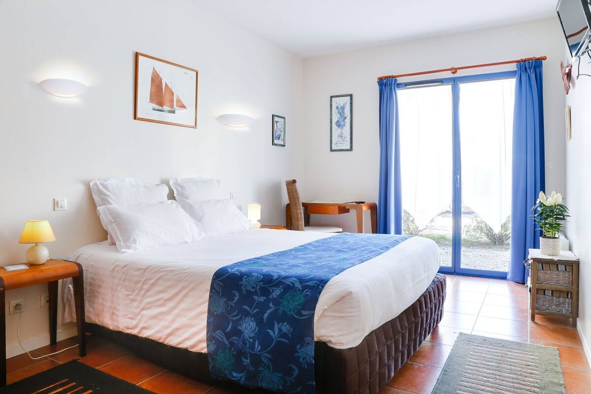 A bedroom with a bed, a desk, a chair, and a window with curtains.