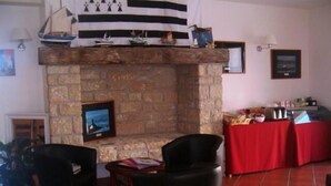 A room with a stone fireplace, a television mounted on the wall, a red table with various items, and two black chairs. - Hôtel le Chevalier Gambette (Saint-Armel)
