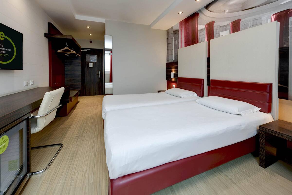 A hotel room with a large bed, a desk with a chair, and a wardrobe.