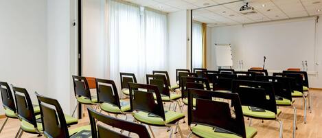 A conference room with rows of chairs, a whiteboard, and a projector on the ceiling.