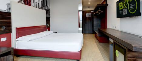 A hotel room with a bed, a desk, and a mirror. There is a staircase leading to an upper level.