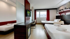 Een hotelkamer met een bureau, twee bedden, een televisie en een raam met gordijnen.