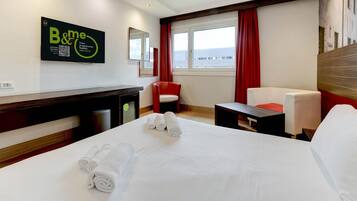 Una camera d'albergo con un letto, due poltrone, un tavolino e una finestra con tende.