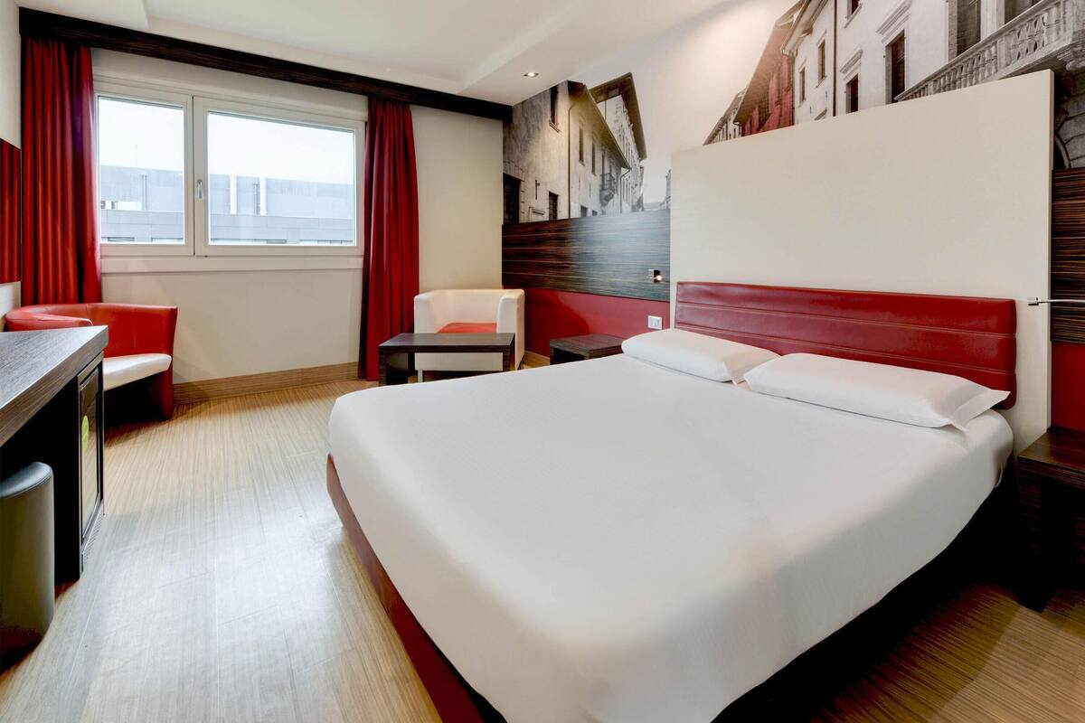 A hotel room with a large bed, a desk, a chair, and a small table.