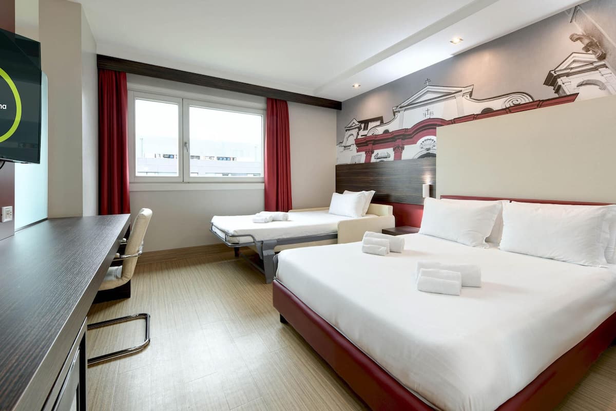 A hotel room with a large bed, a smaller bed, a desk, and a chair.