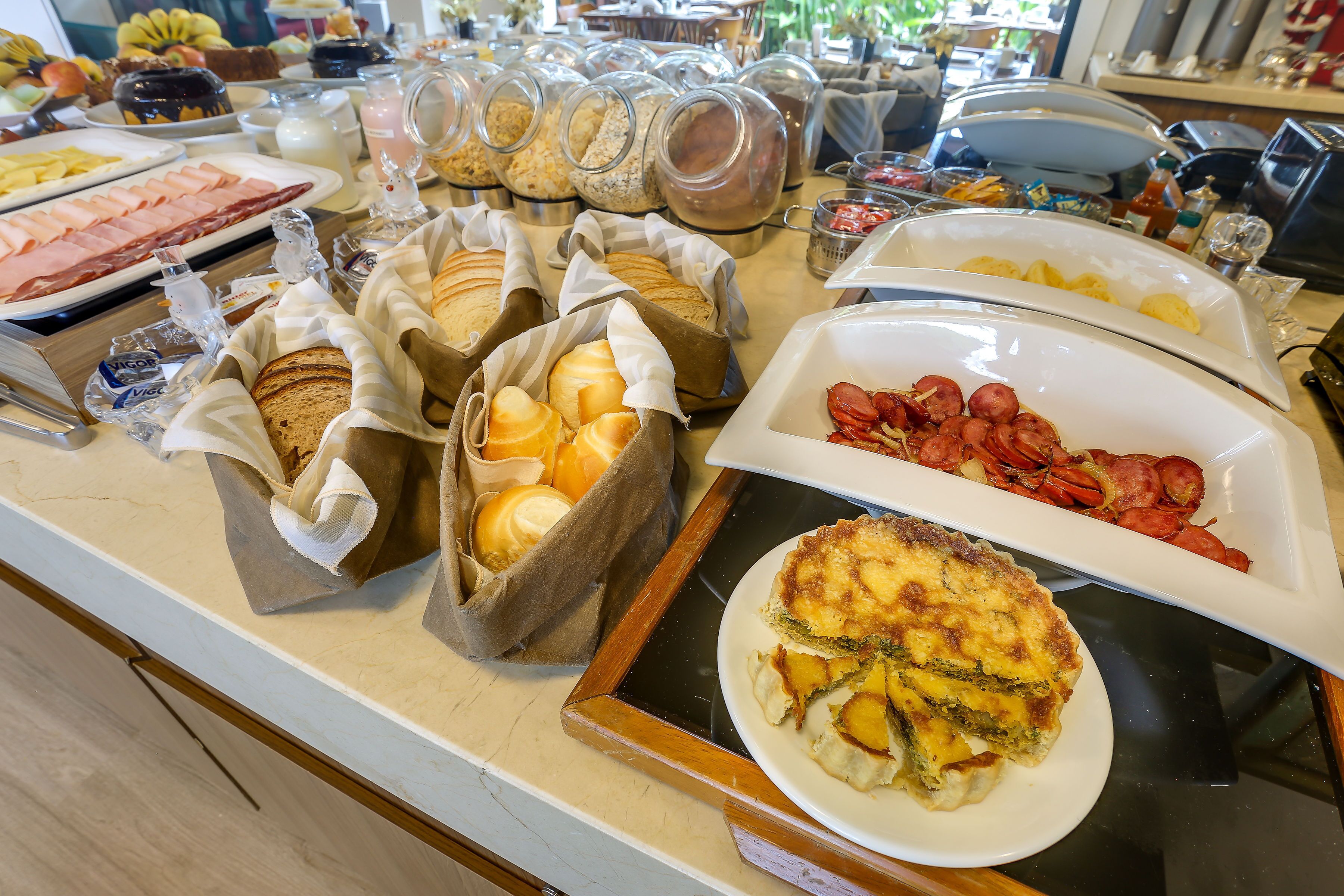 A buffet with various food items including bread, pastries, and a quiche.