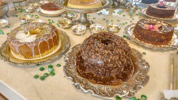 Una mesa con varios pasteles sobre pedestales de plata ornamentados, rodeada de pequeños cuencos y elementos decorativos verdes.
