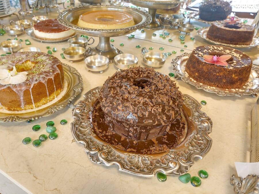 Una mesa con varios pasteles sobre pedestales de plata ornamentados, rodeada de pequeños cuencos y elementos decorativos verdes.