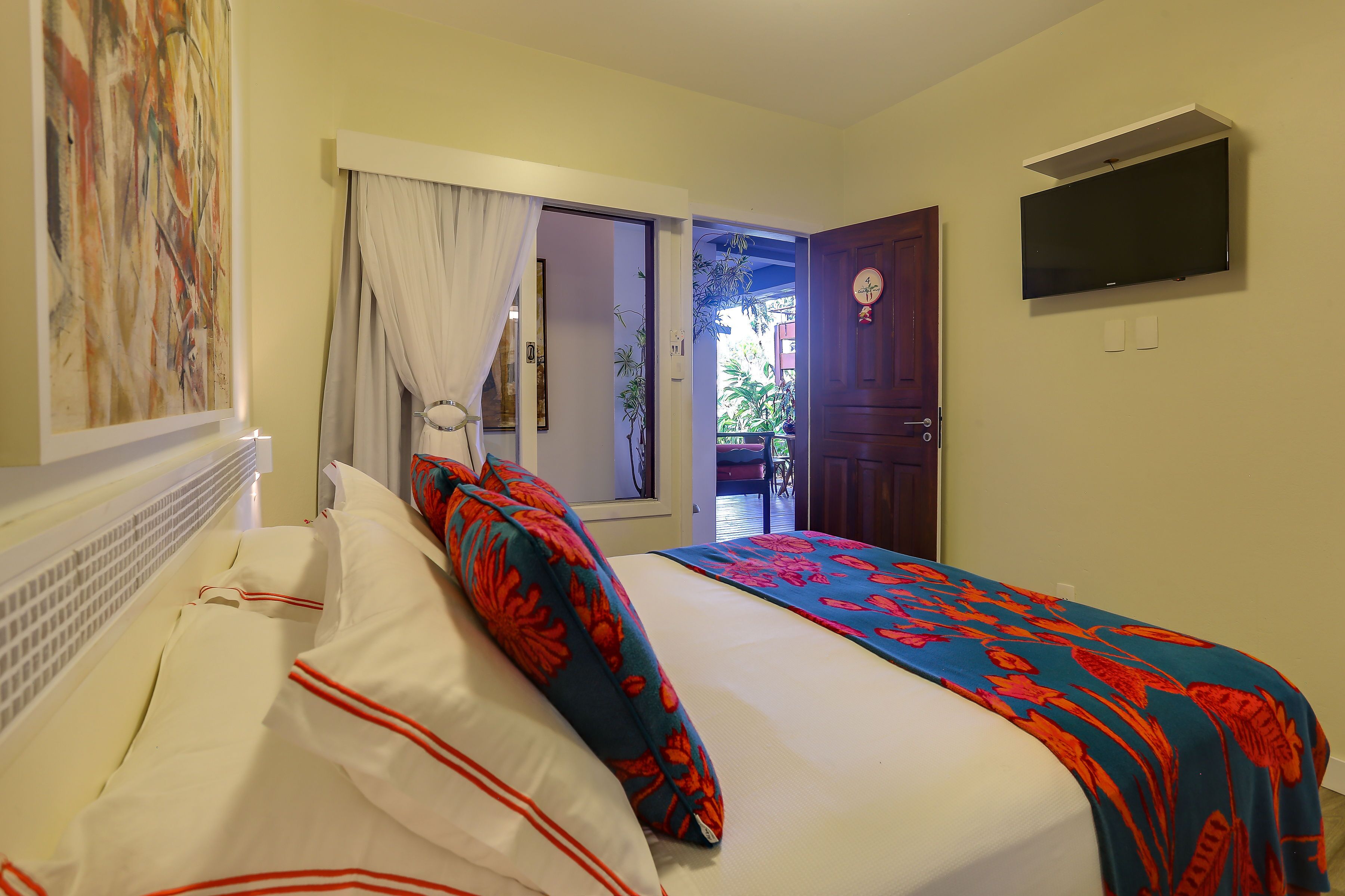 Un dormitorio con cama, televisión instalada en la pared y ventana con cortinas.