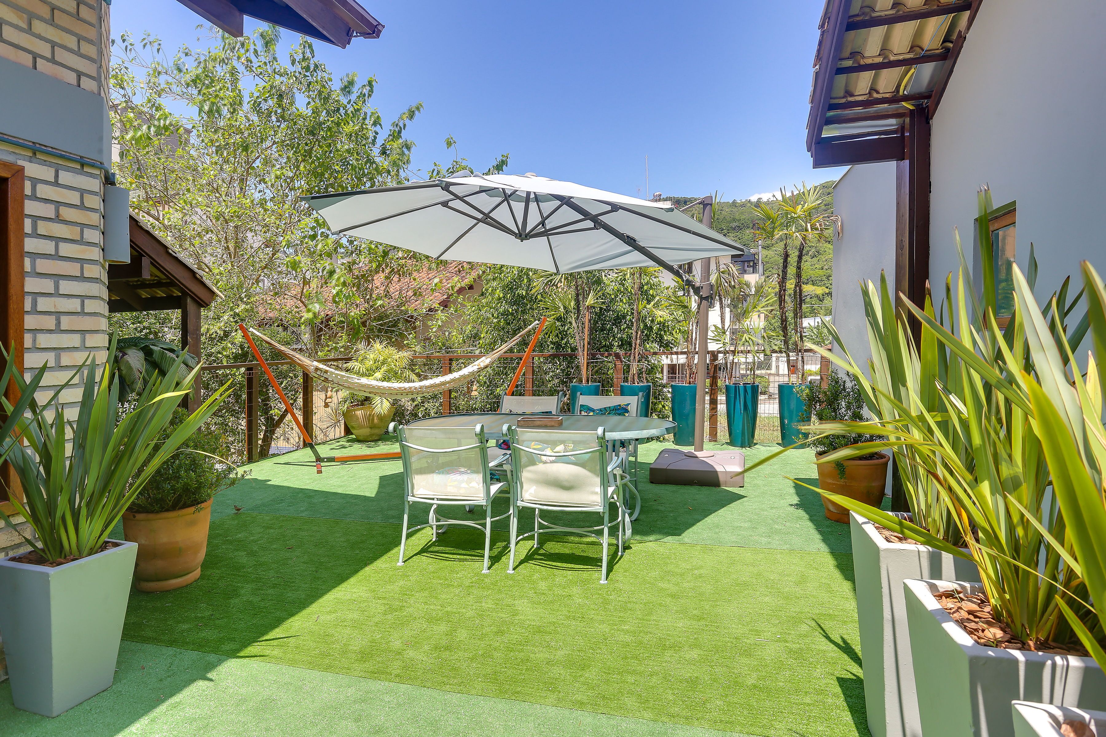 Eine Terrasse mit Kunstgrashalm, einem Tisch mit Stühlen und einem großen Sonnenschirm.